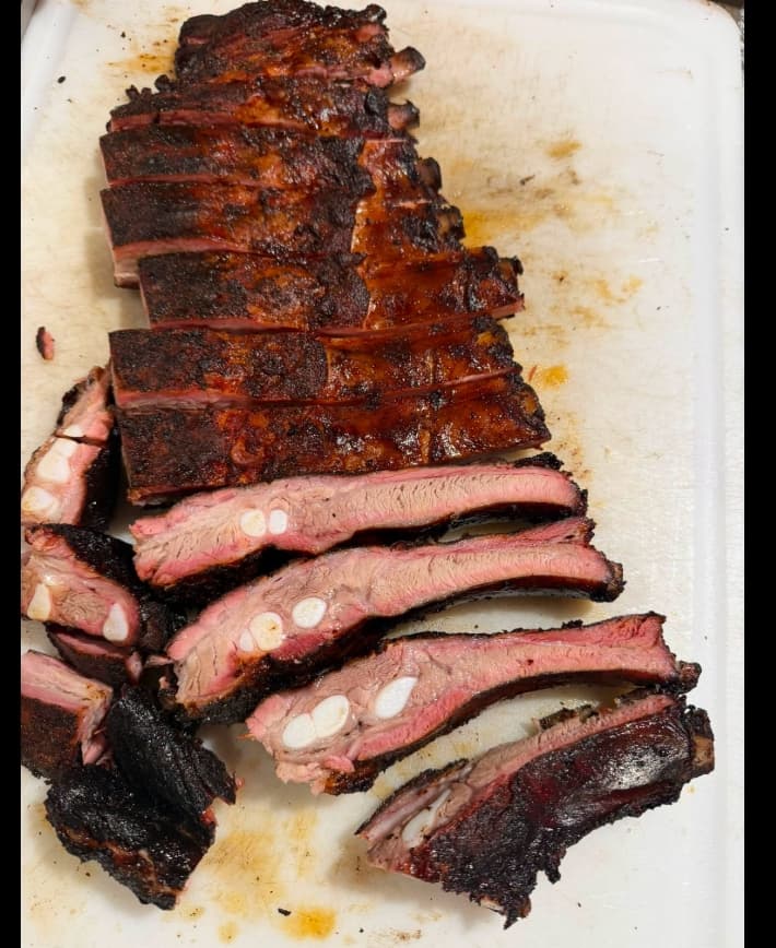 Rack of smoked spare ribs sliced on a board showing a pink smoke ring